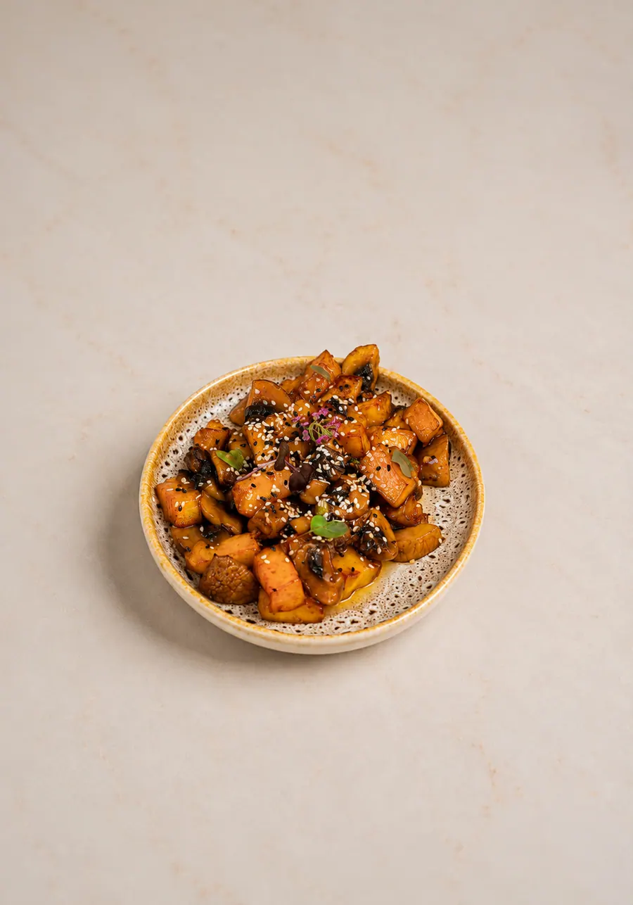 Al Reem seared halloumi: cubes of golden pan-seared halloumi glazed dark with teriyaki and sweet chilli, mixed with mushroom and scattered with white and black sesame seeds, in a shallow speckled bowl.