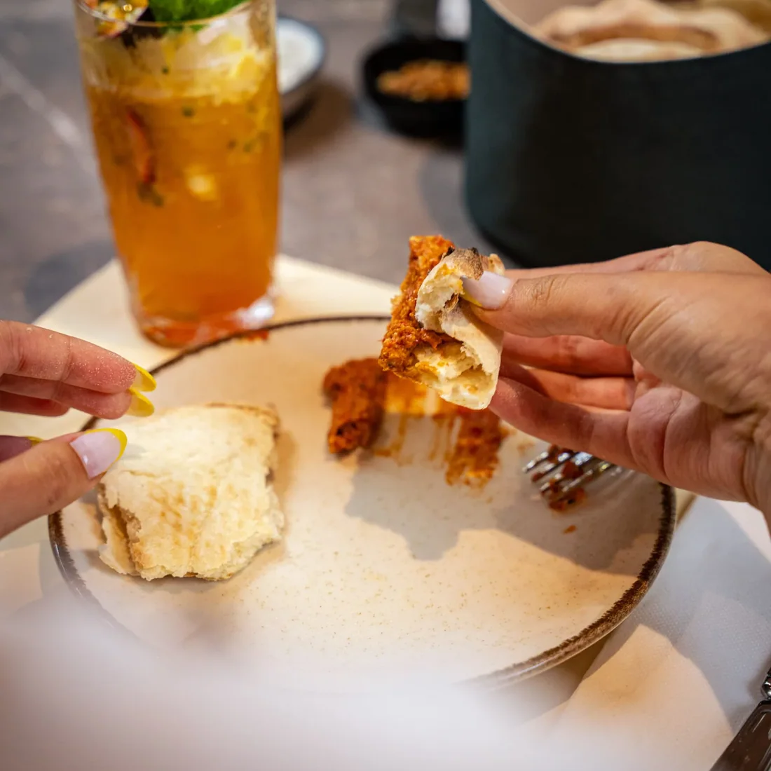 At the table at Al Reem: a hand tearing bread into muhammara, a mocktail with mint beside it.