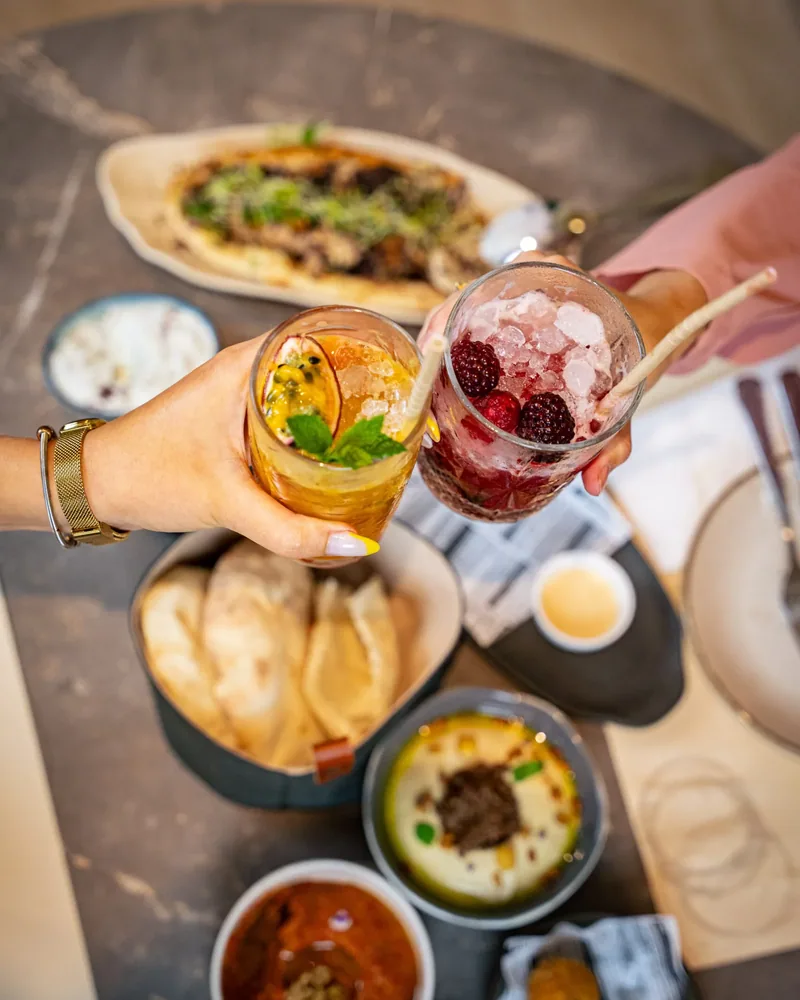 Two mocktails raised over a table of mezze and bread at Al Reem