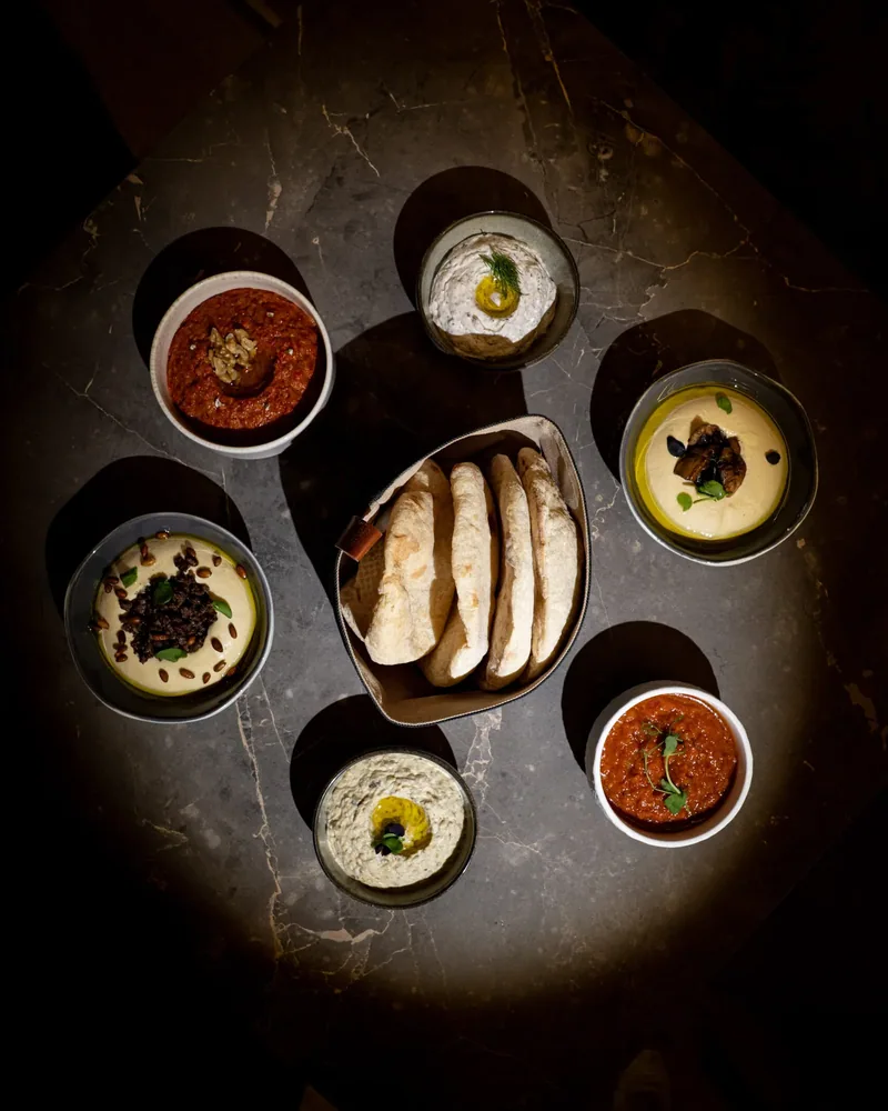 A mezze spread seen from above: dips, pickles and taboon bread on dark marble
